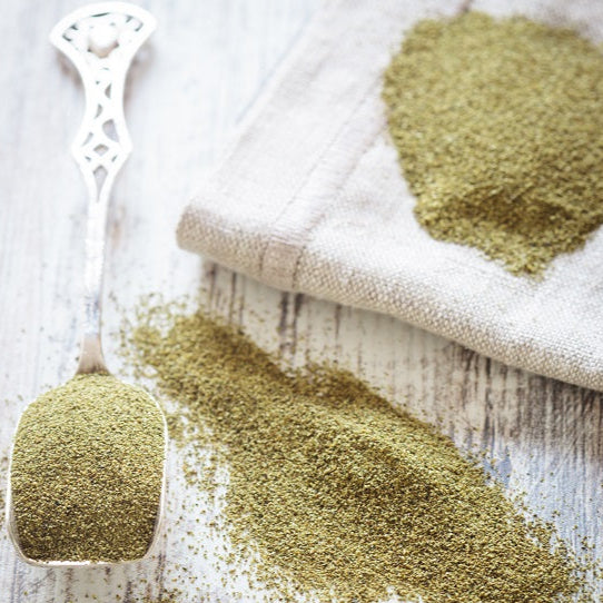 Green spice on a wooden surface with a cloth and measuring spoon.