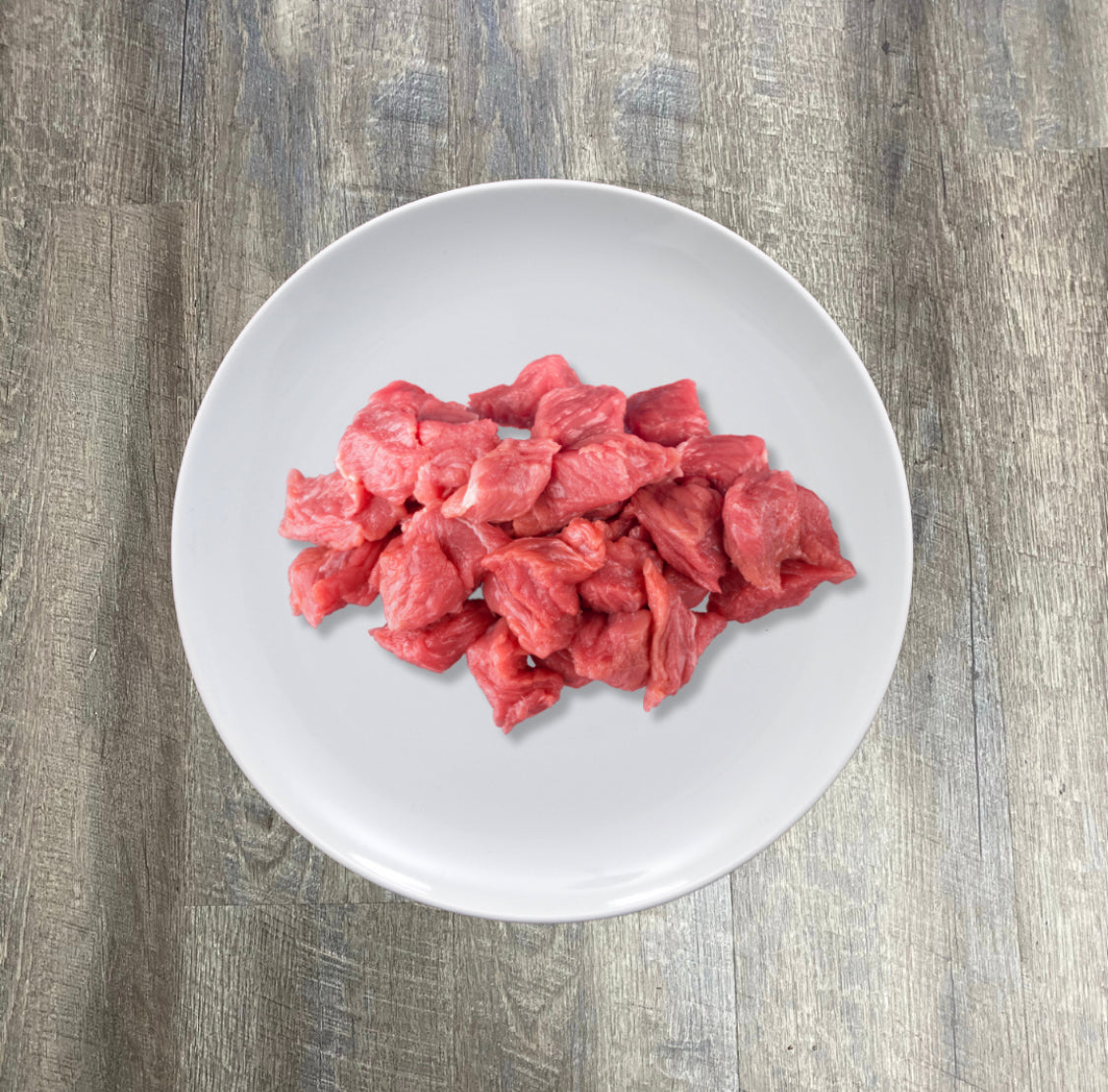 A plate of natural raw beef chunks on a wooden surface.