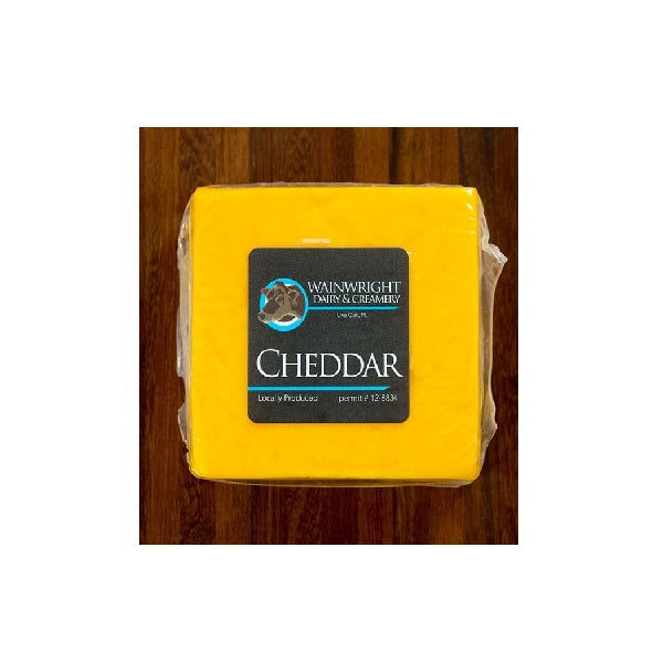 A block of yellow cheddar cheese with the label 'Wainwright' on it, placed on a wooden surface.