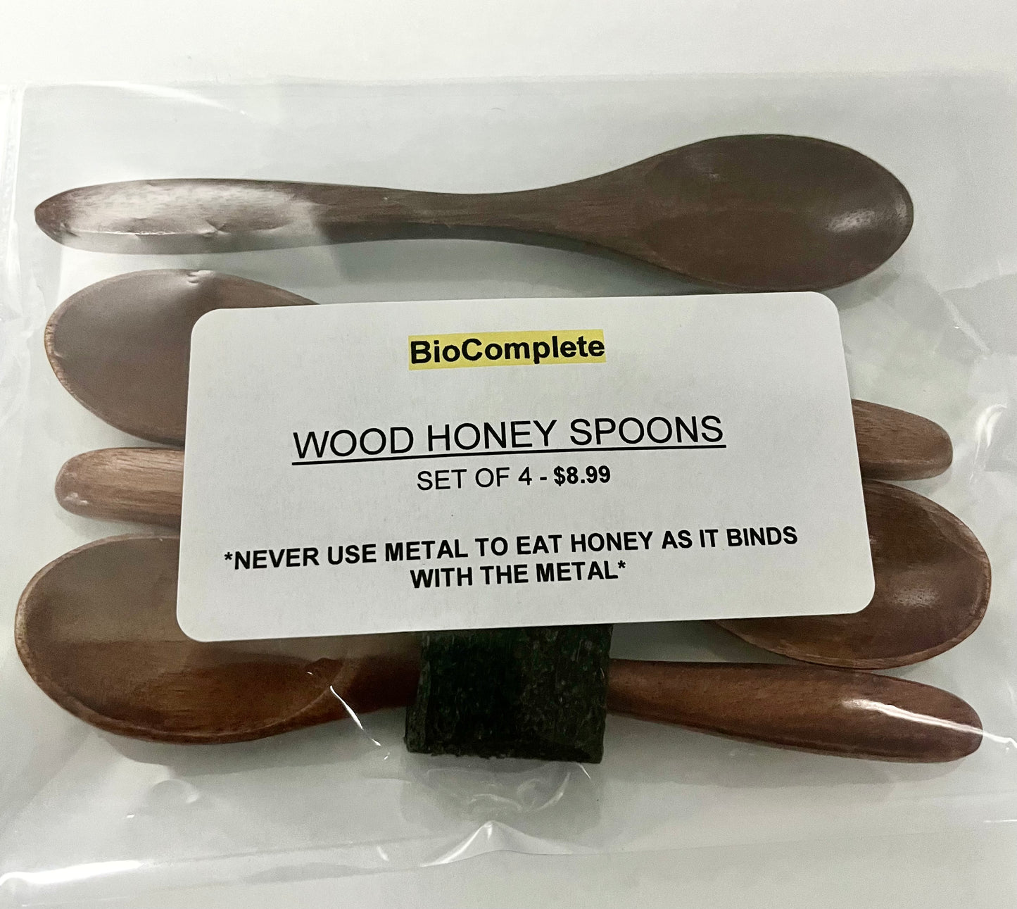 Packaged set of four wooden honey spoons with the brand label 'BioComplete' visible on the packaging.