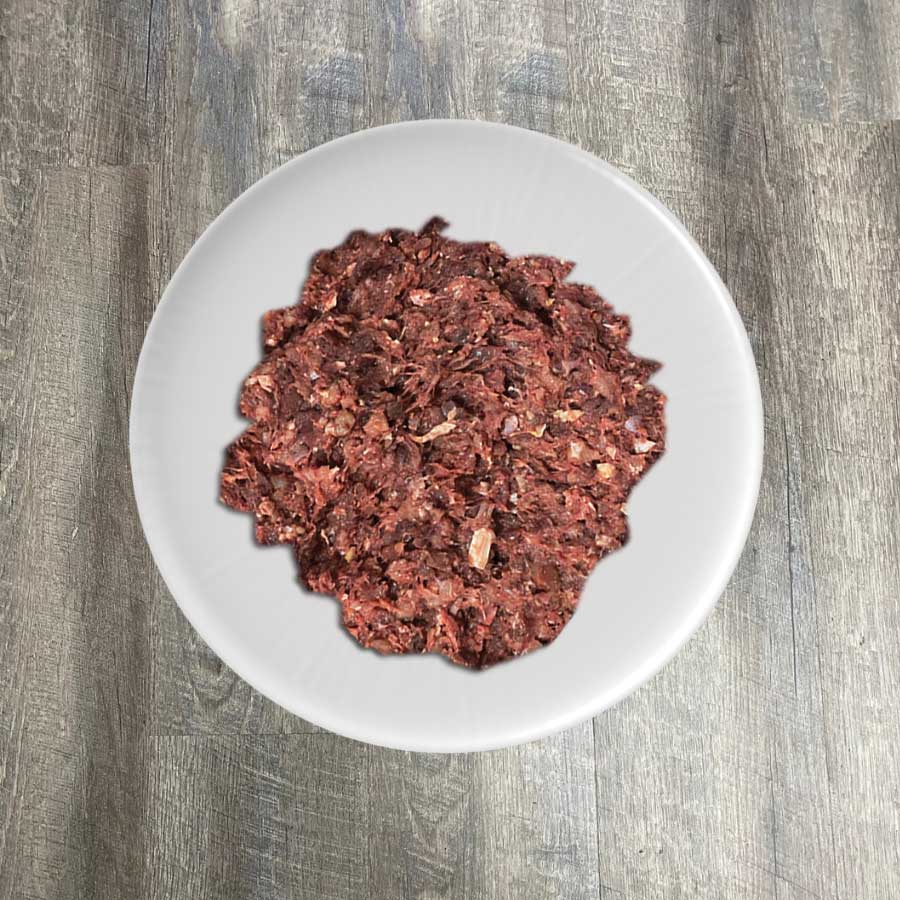 A plate of ground raw turkey meat displayed on a white plate against a wooden background.