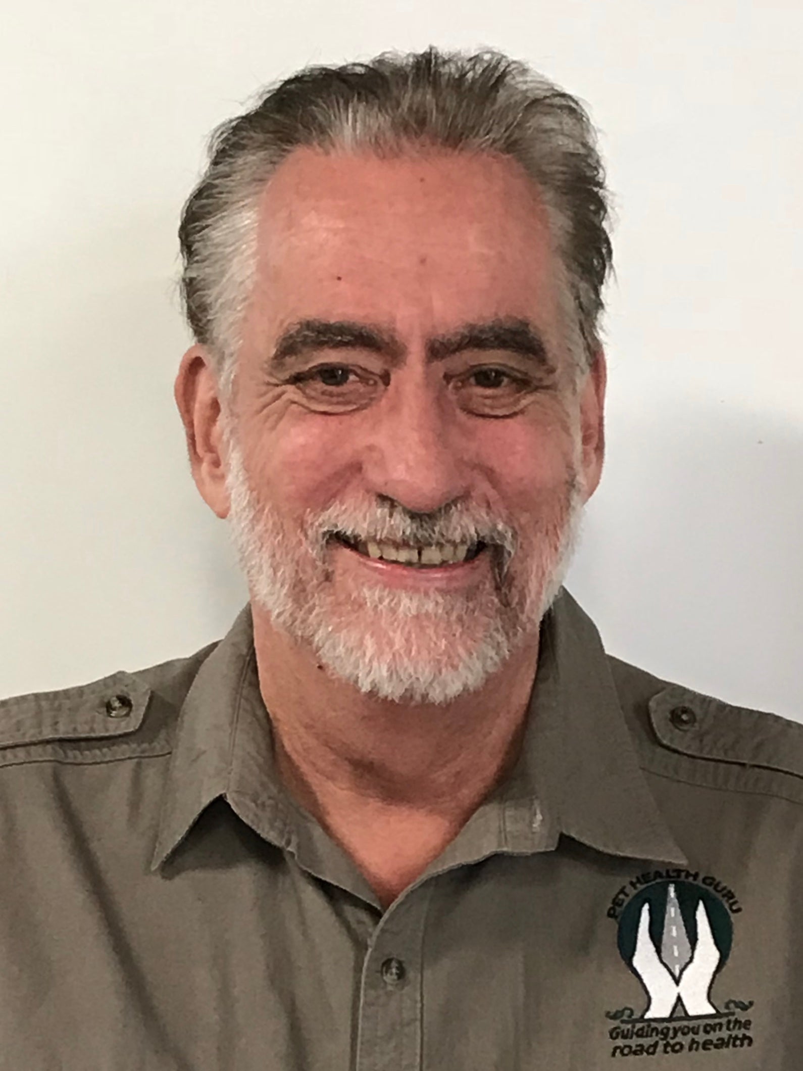 A photo of Bill from My Paleo Pet with a beard and mustache, wearing a button-up shirt, smiling at the camera. The shirt has a logo on the chest.