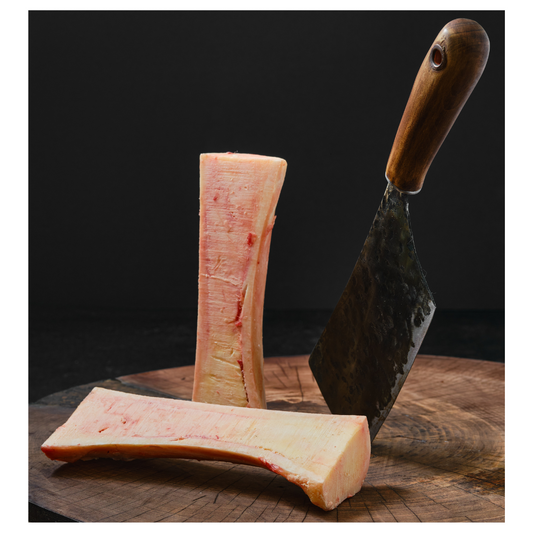 A raw beef marrow canoe cut bone, next to a cutting tool, on a wooden surface.