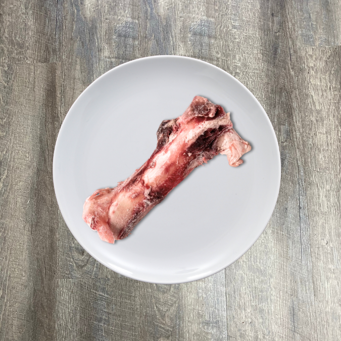 A large, raw, beef marrow bone centered on a white plate with a wooden surface in the background.