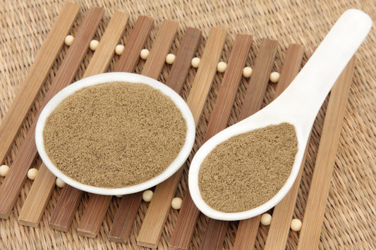 A bowl and a spoon filled with brown powder, placed on a bamboo mat.