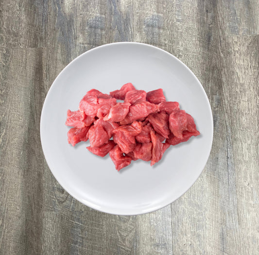 A plate of natural raw beef chunks on a wooden surface.