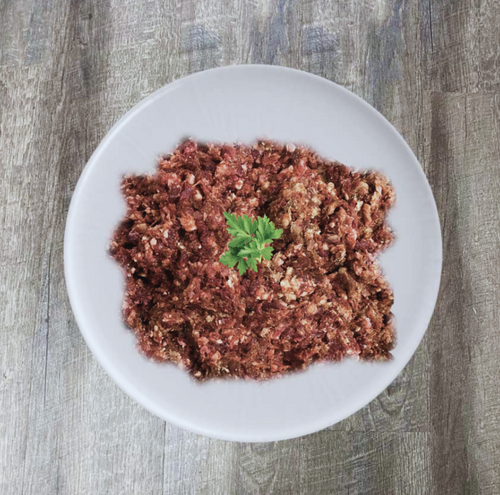 A plate of ground bison meat, likely Bison Ground Purity Grass-fed Organic, presented on a white plate with a green garnish.