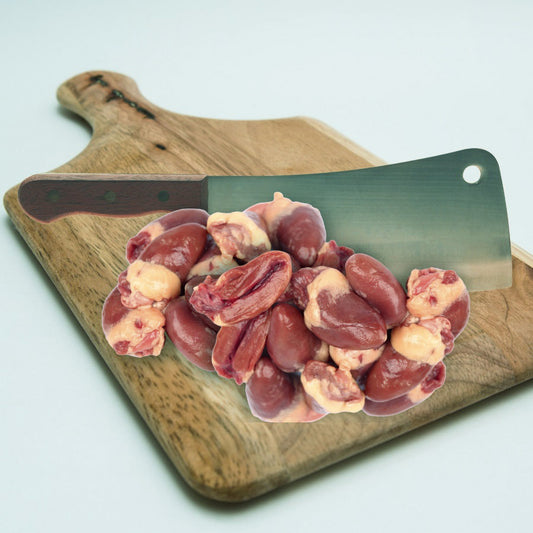 Raw chicken heart chunks on a wooden cutting board with a knife in the background.