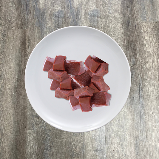 A plate of BioComplete Natural Raw Lamb Liver Chunks on a wooden surface.
