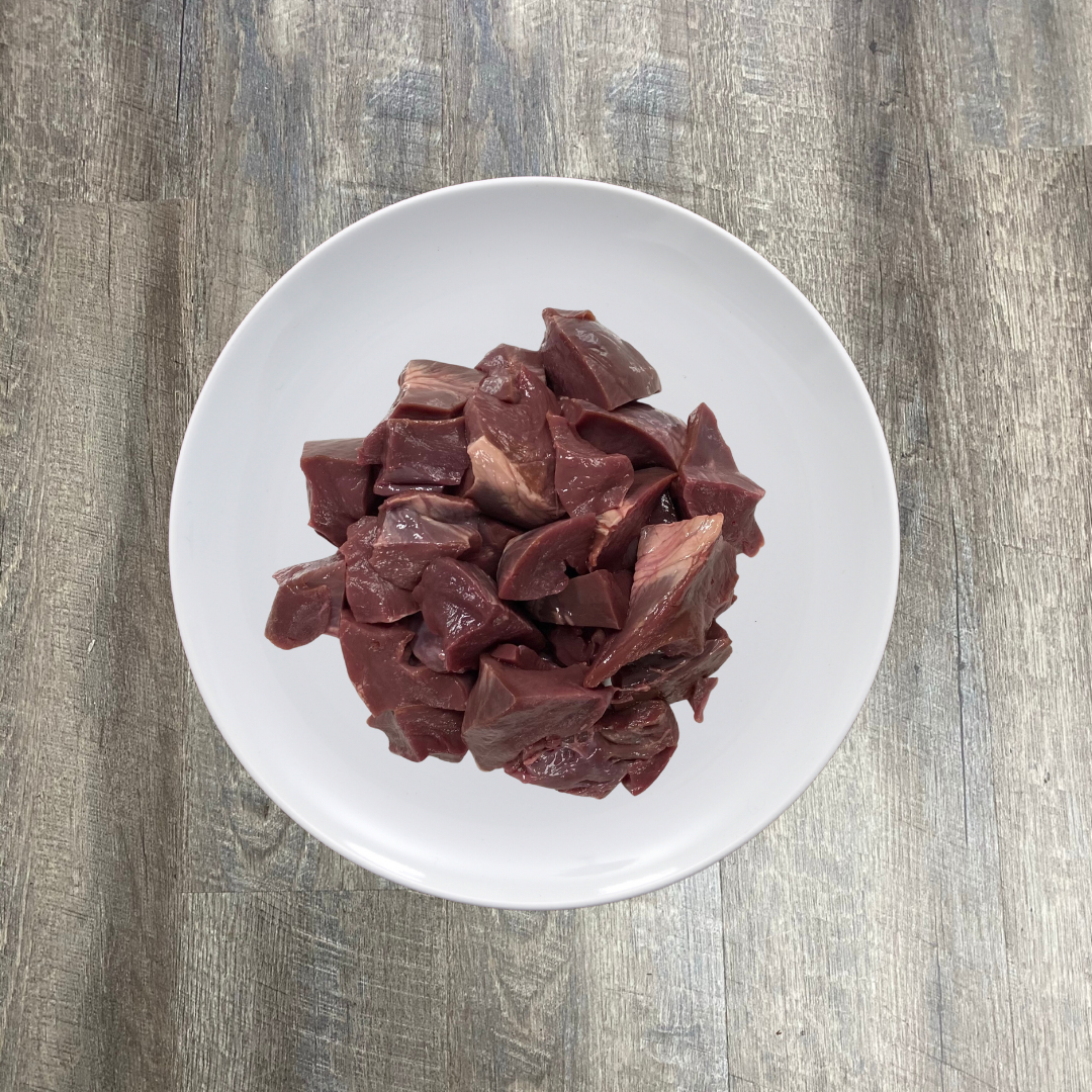 A white plate containing raw chopped pork heart pieces on a wooden surface.