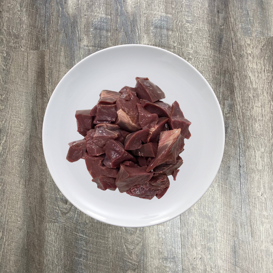 A white plate containing raw chopped pork heart pieces on a wooden surface.
