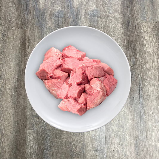 A white plate containing raw pork tenderloin chunks on a wooden surface.