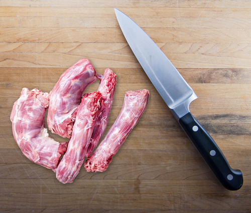 Raw turkey neck chunks next to a kitchen knife on a wooden cutting board.