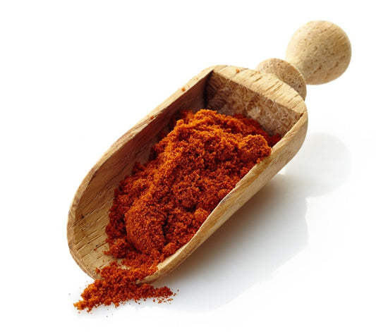 A wooden scoop filled with red paprika powder on a white background.