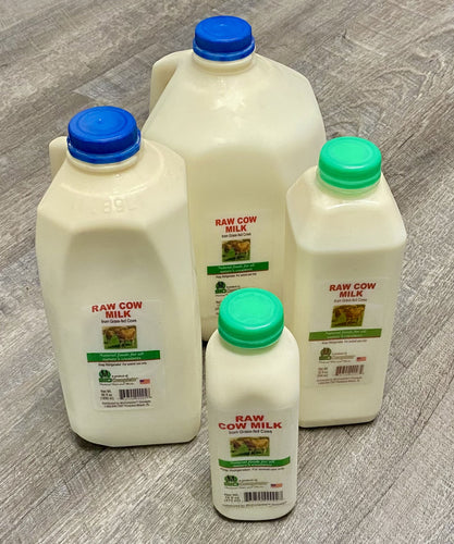 Multiple containers of BioComplete Raw Cow Milk with different sizes, placed on a wooden floor. The containers are labeled and have blue and green caps.