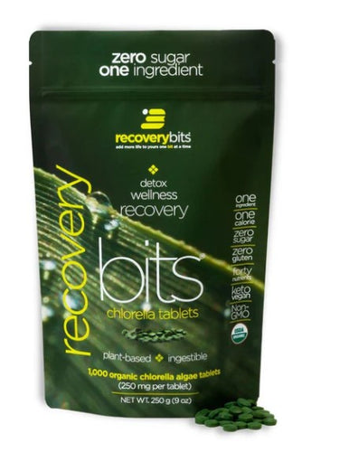 A package of RECOVERYbits® Chlorella tablets with the product visible in front of the package. The package is labeled with 'zero sugar one ingredient' and has various health-related claims.