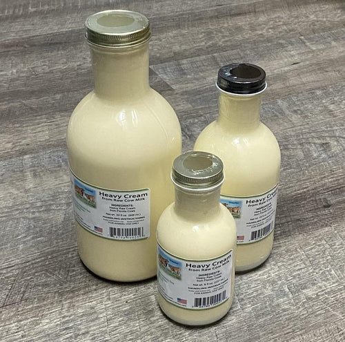 Three glass bottles of varying sizes labeled Heavy Cream, placed on a wooden surface.