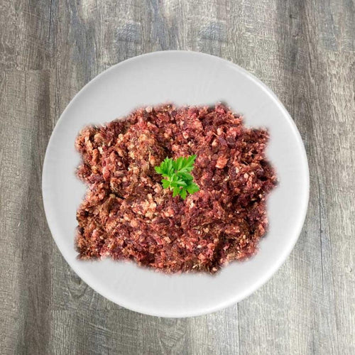 A plate of ground beef with a garnish of parsley on top, placed on a wooden surface.