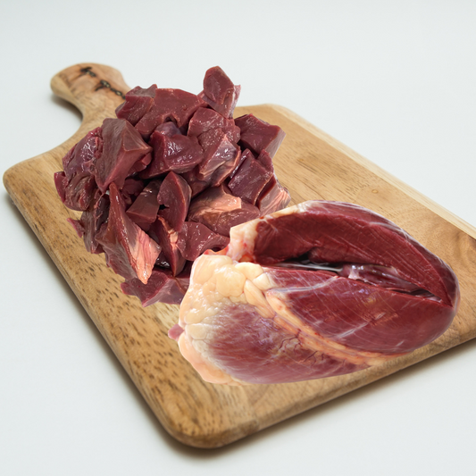 Raw beef heart chunks on a wooden cutting board.