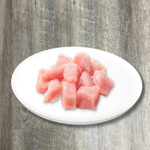 A plate of natural raw chicken breast chunks on a wooden surface.