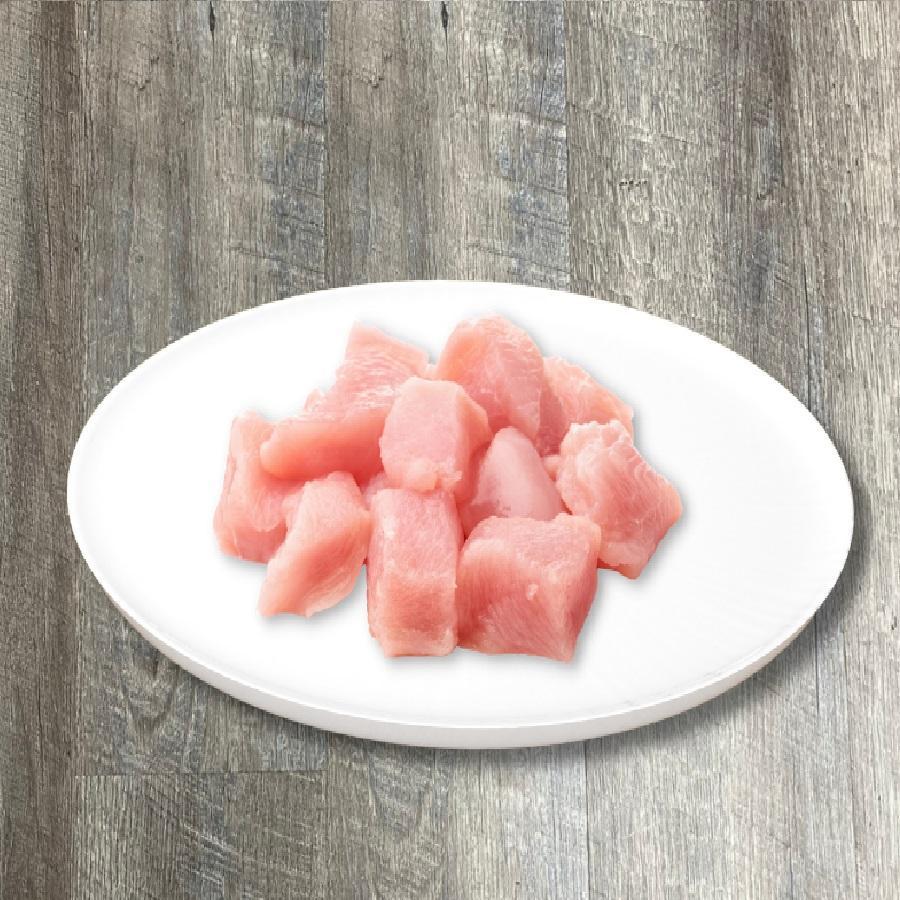 A plate of natural raw chicken breast chunks on a wooden surface.