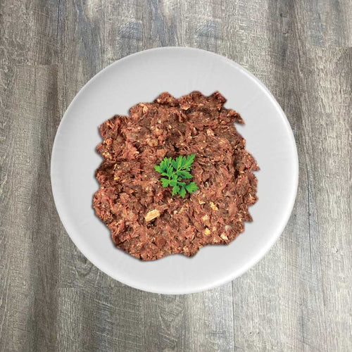 A bowl of ground natural raw chicken mix, presumably the product mentioned, garnished with a leaf of parsley on a wooden surface.