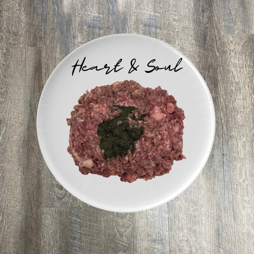 A plate of ground pork meat with visible pieces of herbs or spices, placed on a wooden surface, with the words 'Heart & Soul' written above it.
