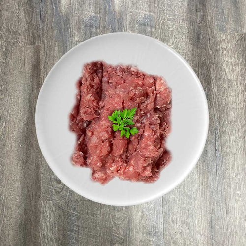 A plate of raw ground rabbit meat, with a sprig of parsley on top, placed on a wooden surface.