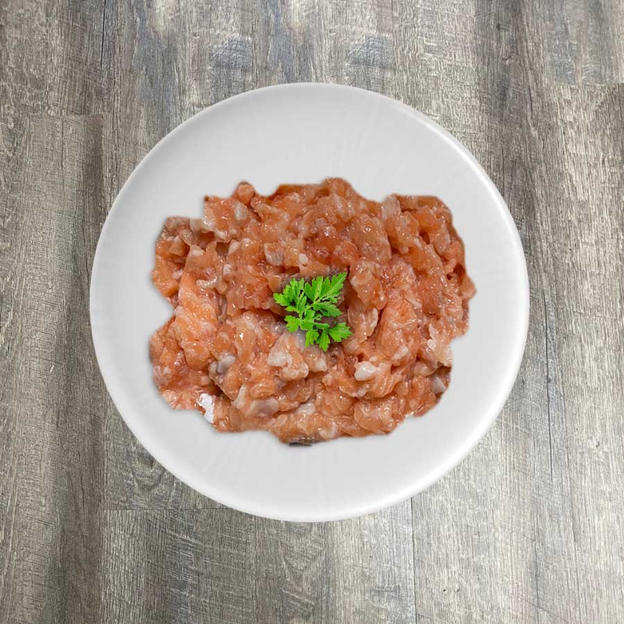 A bowl of raw ground salmon on a plate, with a sprig of parsley for garnish, on a wooden surface.