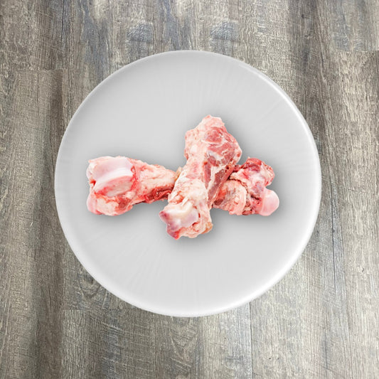 Raw pork marrow femur bones on a white plate.