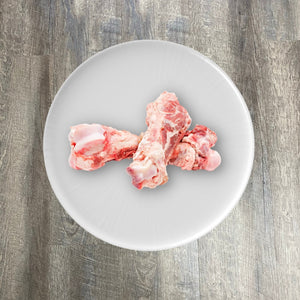 Raw pork marrow femur bones on a white plate.