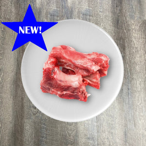 Raw pork rib bones on a white plate with a blue star label indicating 'NEW' on the top left corner.